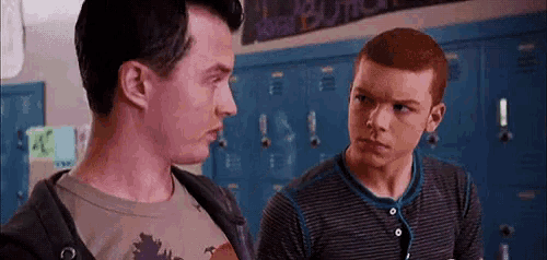 two young men are standing next to each other in front of blue lockers in a school hallway .