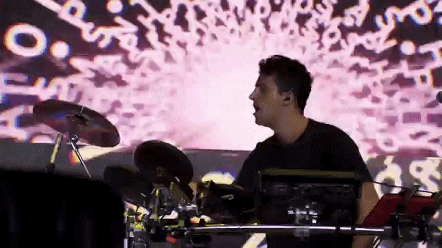 a man in a black shirt is playing drums in front of a screen that says ' o. ' on it