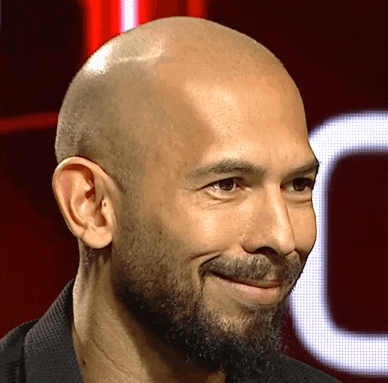 a bald man with a beard smiles in front of a red background