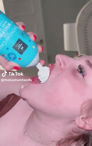a woman is eating whipped cream from a can that says birthday cake on it