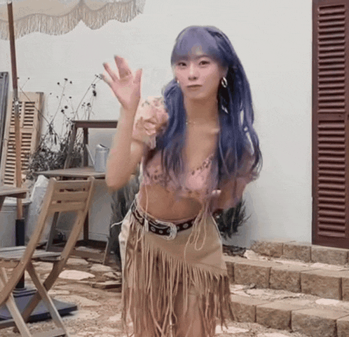 a woman with purple hair wearing a fringed skirt is waving