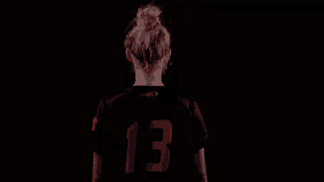 a woman wearing a campbell jersey stands in the dark with her arms crossed
