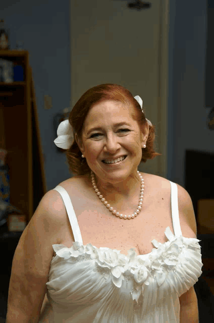 a woman wearing a white dress and a pearl necklace smiles