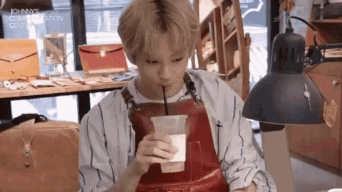 a man wearing an apron drinking through a straw from a cup with johnny 's communication center in the background