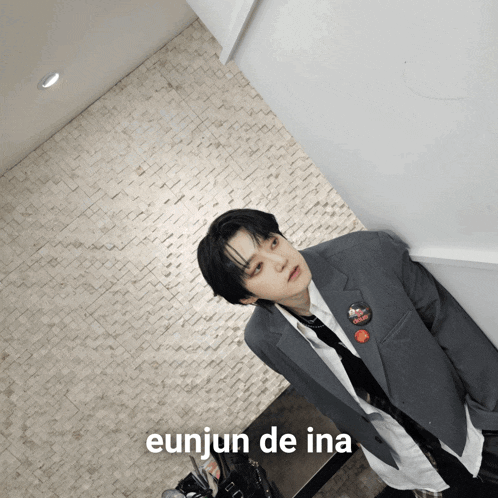 a man in a suit and tie is leaning against a wall with the words " eunjun de ina " on the bottom