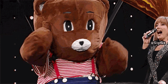 a woman singing into a microphone next to a teddy bear