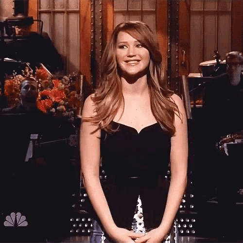 a woman in a black dress is smiling in front of a nbc sign
