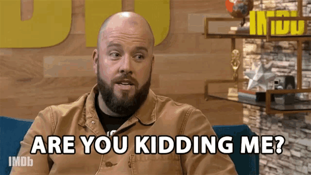 a man with a beard is sitting in a chair and asking are you kidding me ?