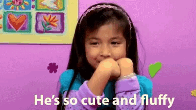 a little girl is biting her nails and saying he 's so cute and fluffy