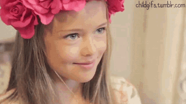 a little girl wearing a pink flower crown is smiling for the camera