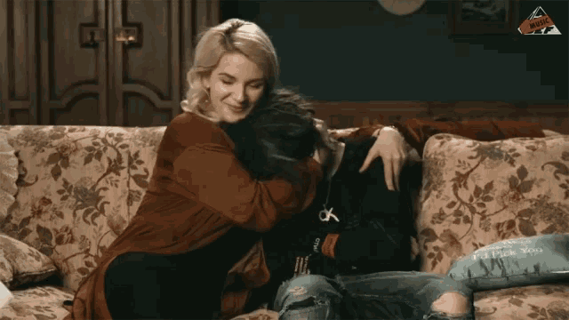 a woman sitting on a couch hugging another woman who is wearing a ck shirt