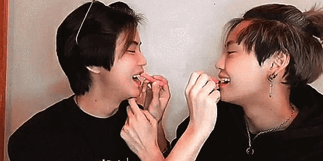 two young men are eating candy from each other 's hands .