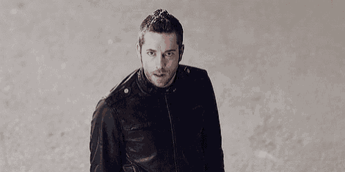 a man in a black leather jacket is standing in front of a wall .