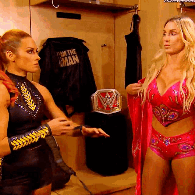 two women are standing in a locker room and one has a wwe belt on her