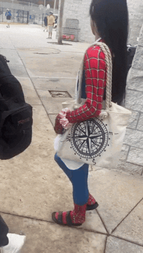 a woman in a spiderman costume is carrying a tote bag that says e on it