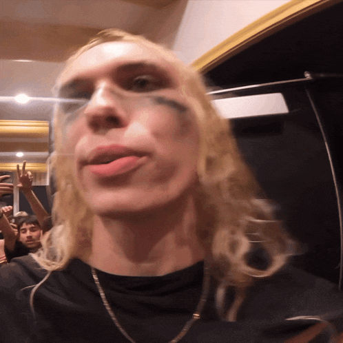 a man with long blonde hair making a peace sign in front of a crowd