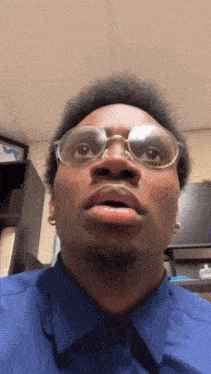 a man wearing glasses and a blue shirt is making a surprised face