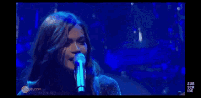 a woman is singing into a microphone on a stage with a blue background .