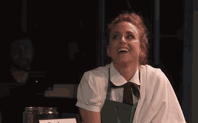 a woman wearing a green apron and white shirt smiles