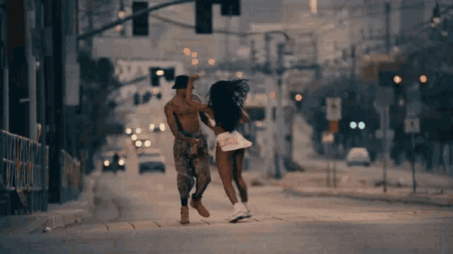 a man and a woman are dancing on a street with a sign that says no smoking