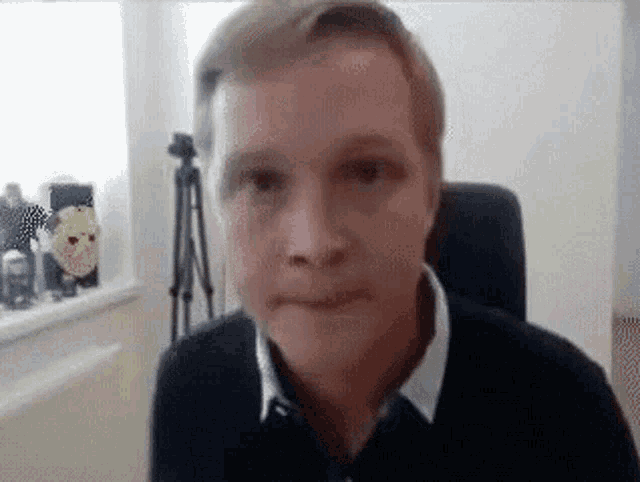 a man is sitting in a chair looking at the camera with a tripod in the background .