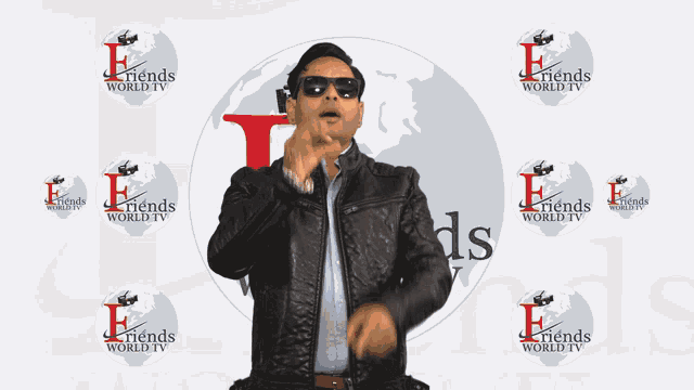 a man wearing sunglasses and a leather jacket stands in front of a wall that says friends world tv