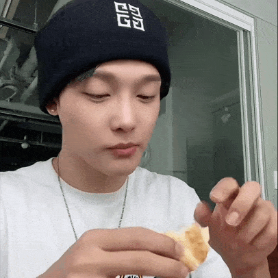 a young man wearing a beanie and a white shirt is eating a piece of food .