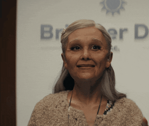 an older woman stands in front of a sign that says briller