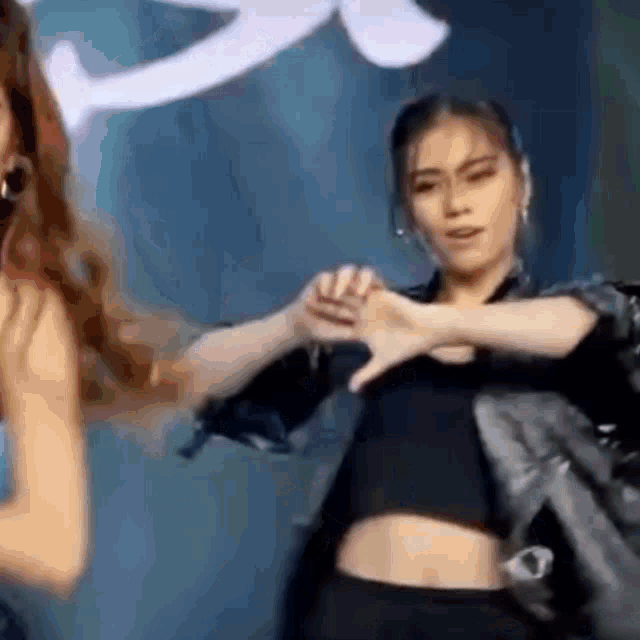 a woman in a black crop top is dancing with another woman in a black jacket .