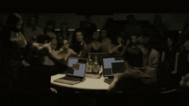 a group of people sit around a table with laptops