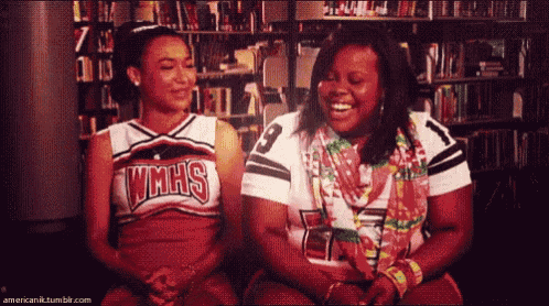 two cheerleaders wearing vmhs uniforms sit next to each other in a library