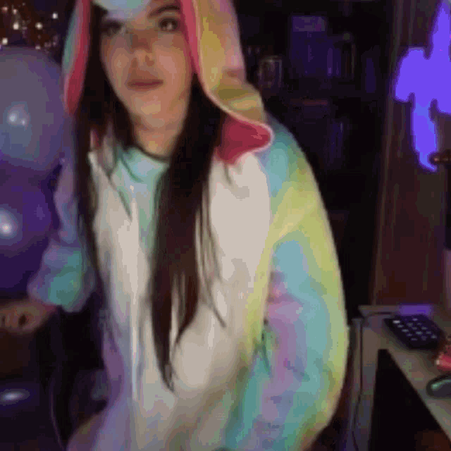 a woman wearing a unicorn hoodie is standing in front of a computer desk .