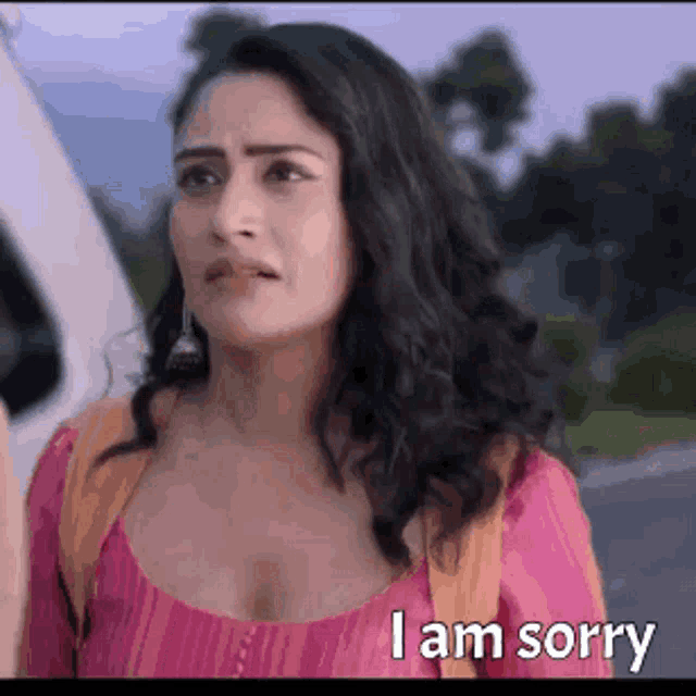 a woman in a pink shirt is standing next to a car and says i am sorry .