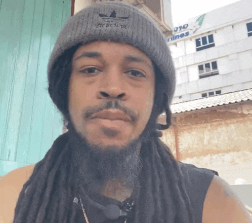 a man with dreadlocks is wearing a grey adidas beanie