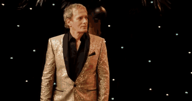 a man in a gold tuxedo stands in front of a microphone