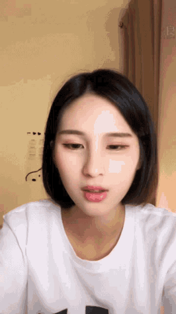 a woman with short black hair is wearing a white t-shirt with the letter t on it