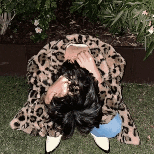 a woman wearing a leopard print coat is sitting on the grass