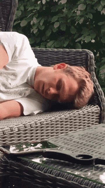 a young man is laying on a wicker chair