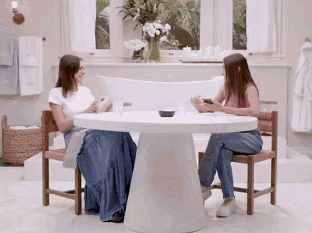 two women sit at a table in a bathroom with a bowl on it