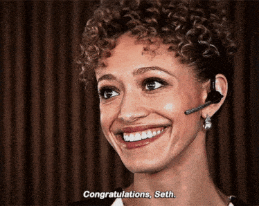 a woman with curly hair wearing a headset is smiling and saying congratulations , seth .
