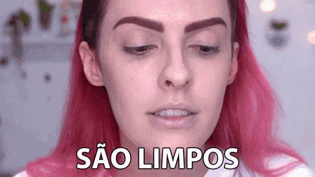 a woman with pink hair is making a funny face and the words sao limpos are written on her face .