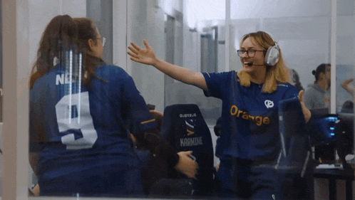 a woman wearing an orange shirt high fives another woman in a blue shirt