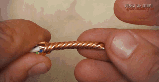 a close up of a person 's hand holding a twisted copper wire with russian writing in the corner