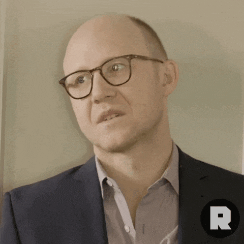 a man wearing glasses and a suit has a letter r on the bottom