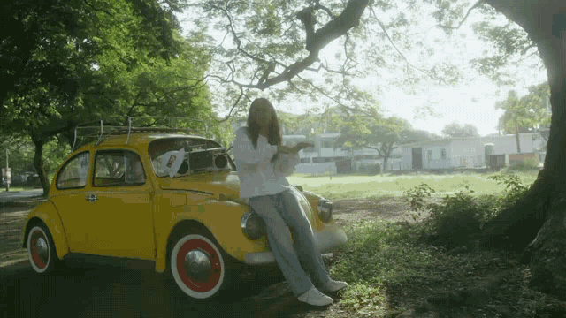 a woman sits on the back of a yellow car with a boombox on the roof