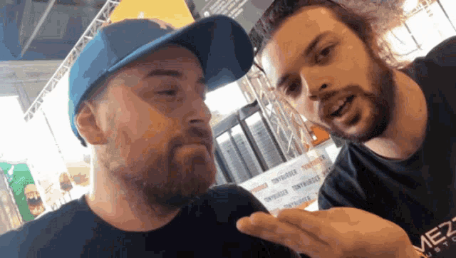a man wearing a blue hat is talking to another man wearing a shirt that says mezz