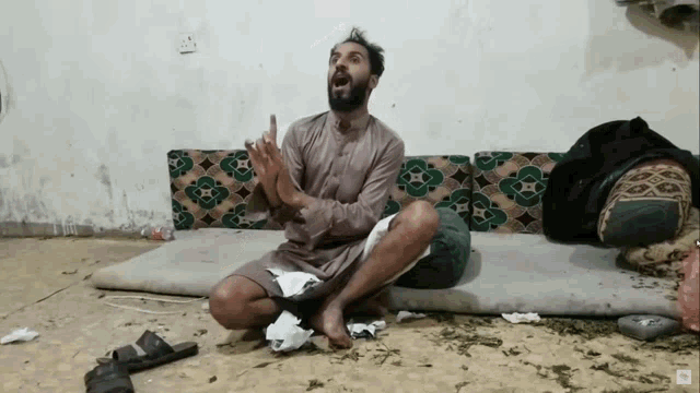 a man with a beard is sitting on the floor with his hands in his pockets