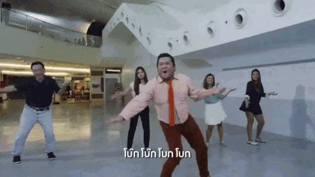 a group of people are dancing in a hallway with a man wearing a pink shirt and orange tie