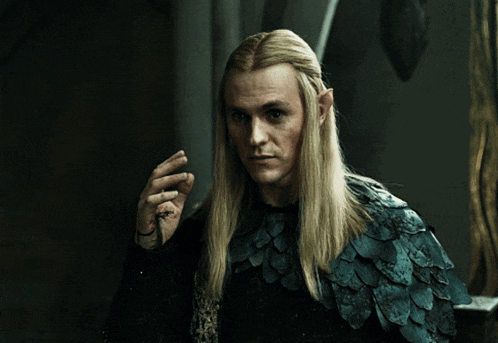 a man with long blonde hair is wearing a blue feathered cape and waving his hand