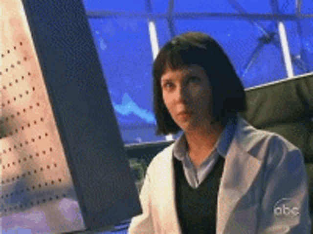 a woman in a lab coat is sitting in front of a computer screen that says abc on it